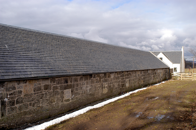 Faldón continuo de pizarra natural sobre el muro de piedra de una nave en Dalmeny Steading, Escocia